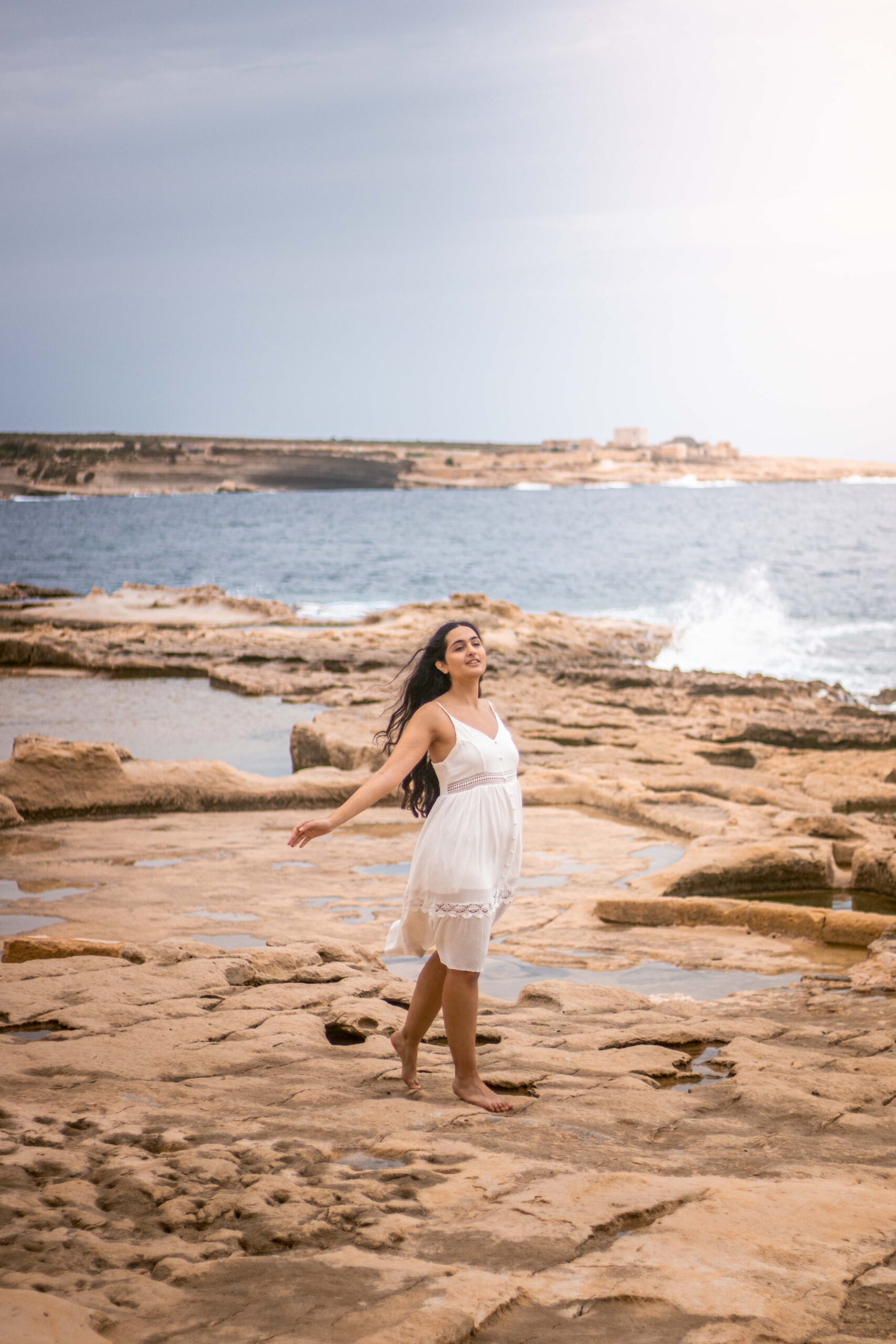 Woman wearing a white dress standing in the old salt-making pans of the Il-Qali hiking area located near Saint Peter's Pool in Malta