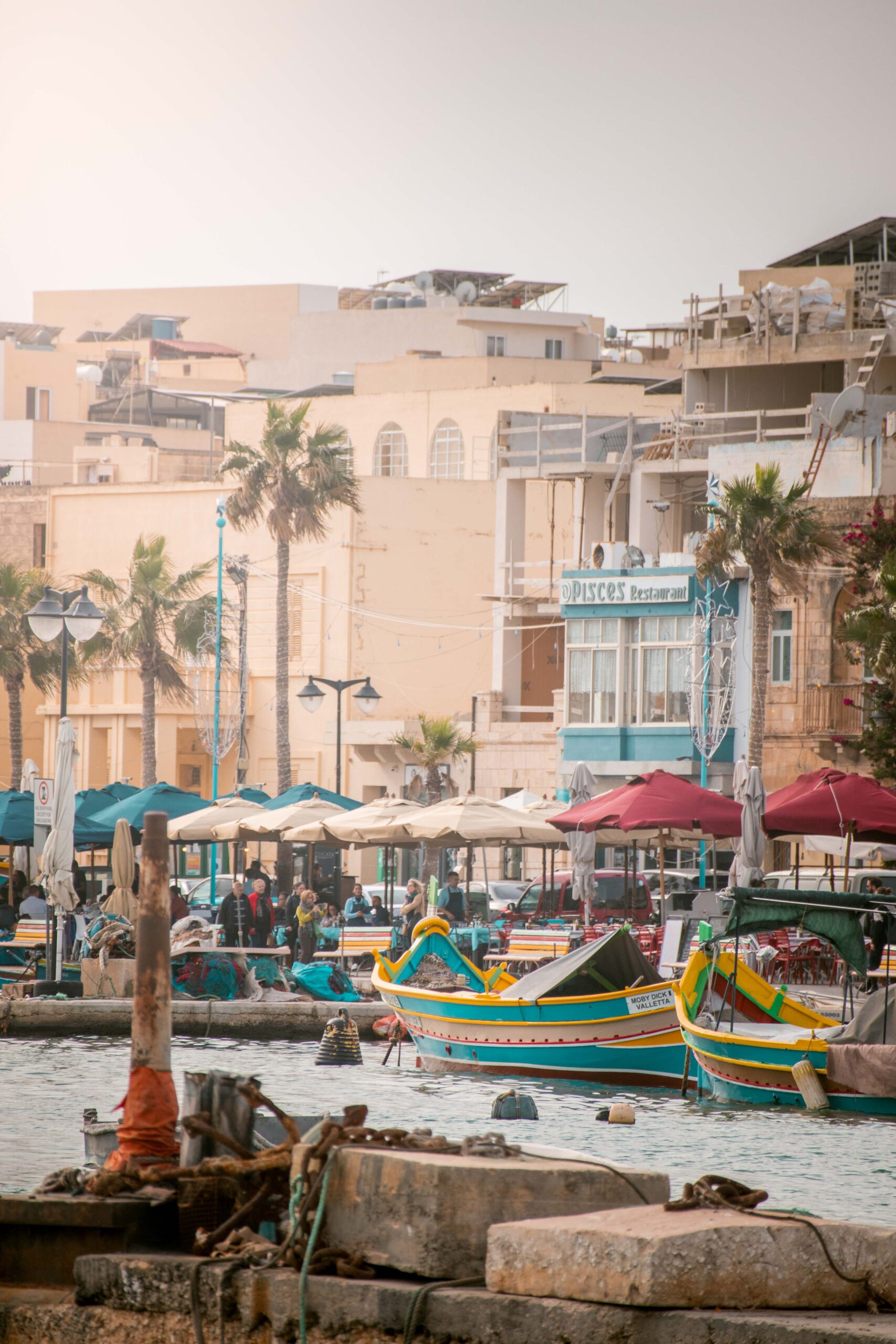 Sunday fish market and traditional colourful luzzu boats near the waterfront of Marsaxlokk, Malta