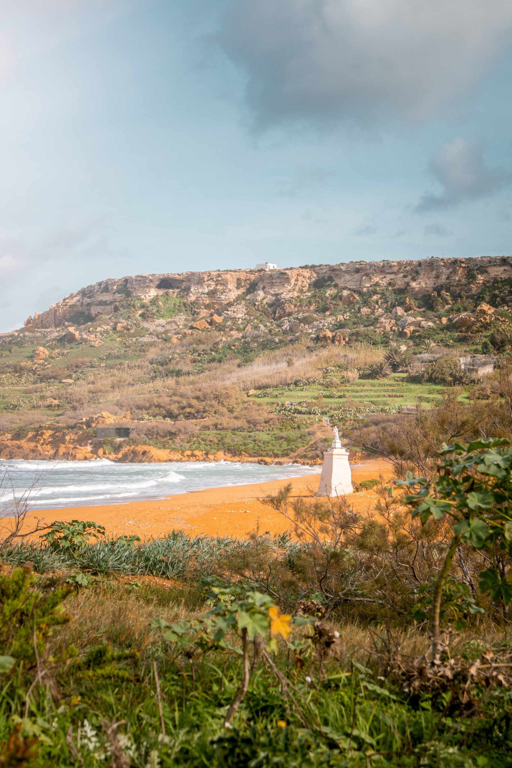 View of Ramla Bay Beach on Gozo island, Malta featuring orange-red sand, statue of Our Lady of Hope and Tal-Mixta Cave