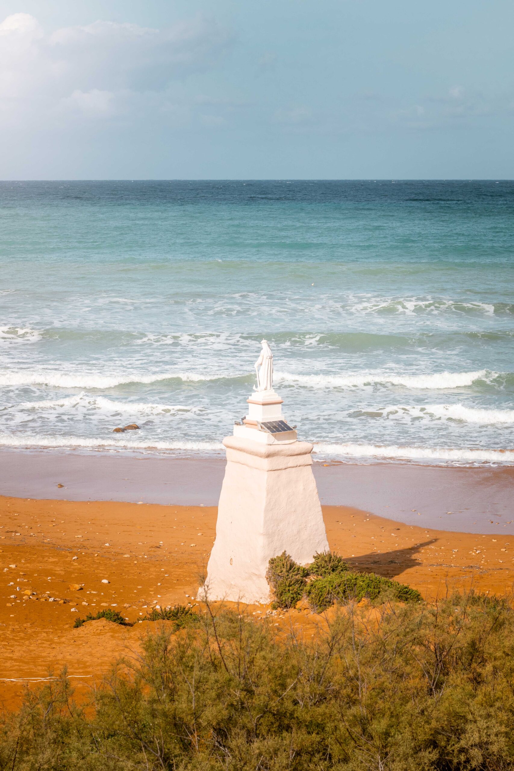 Orange-red sand and Landmark statue of Our Lady of Hope in Ramla Bay Beach on Gozo island, Malta