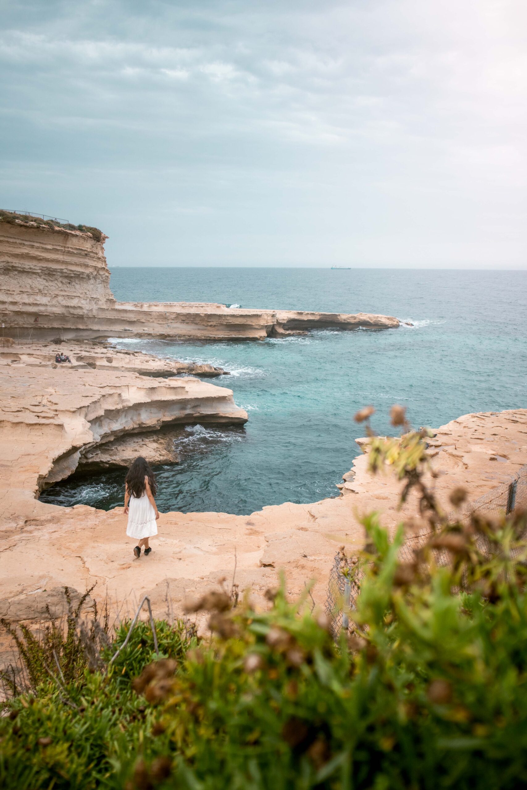 Woman wearing a white dress walking near the edge of Saint Peter's Pool in Malta