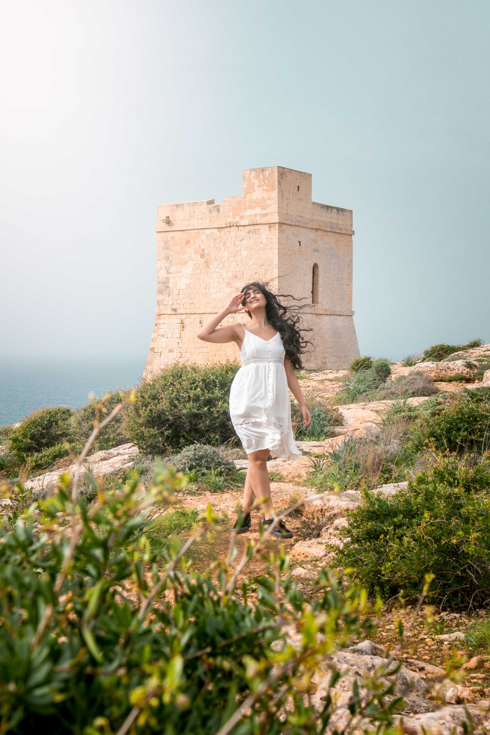Woman wearing white dress standing in front of Ħamrija Coastal Tower in Malta