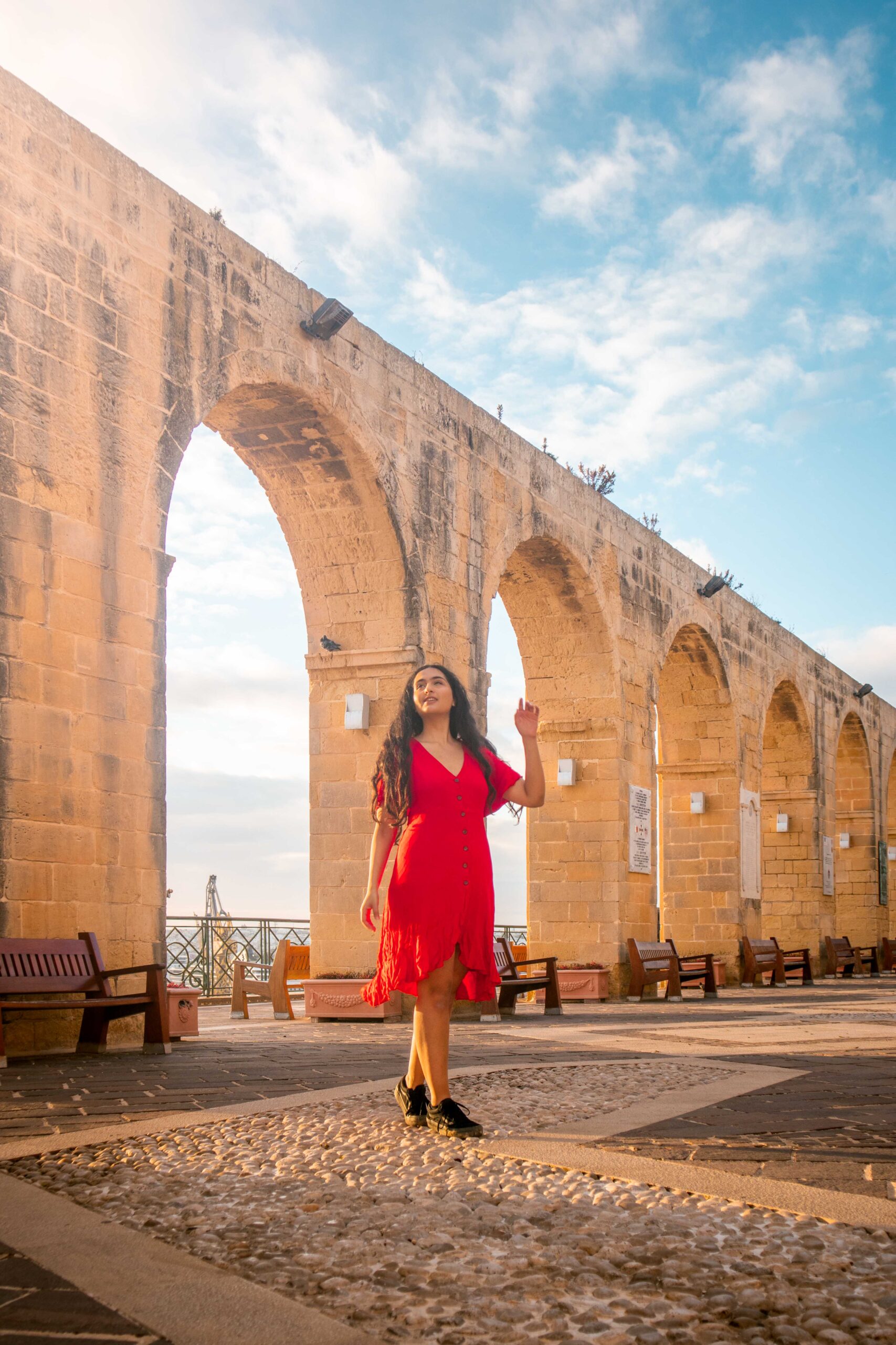 Woman wearing a red dress in front of the arches of the Upper Barrakka Gardens of Valletta, Malta