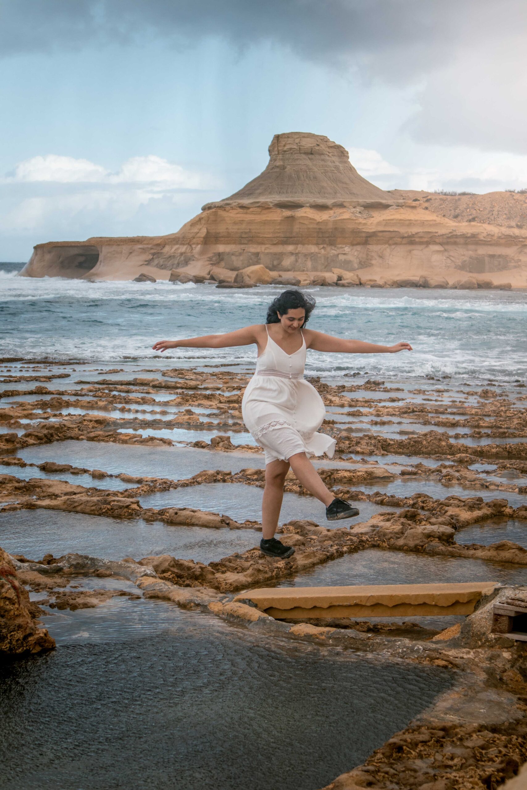Woman wearing a white dress standing in Xwejni Salt Pans with a view in Xwejni Rock on Gozo island, Malta