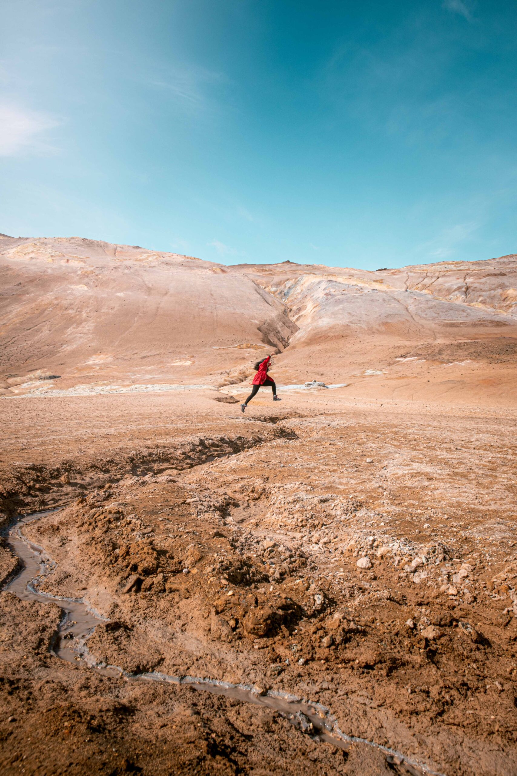 Woman jumping in Hverir (Hverarönd) geothermal area in front of Námafjall ridge near Lake Mývatn, North Iceland