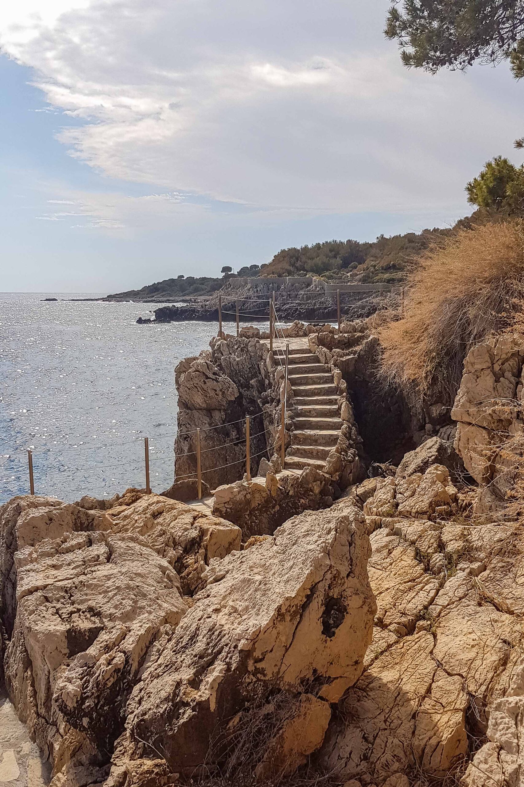 Staircase, rocks, and view of the Mediterranean Sea along the Sentier du Littoral hiking trail during a sunny day in Antibes, France