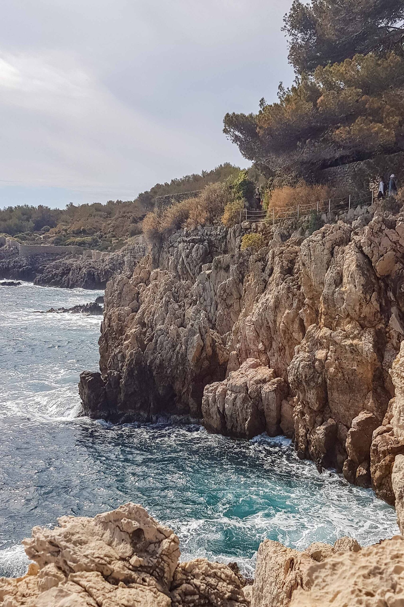 Rock cliffs and blue waves along the Sentier du Littoral hiking trail during a sunny day in Antibes, France