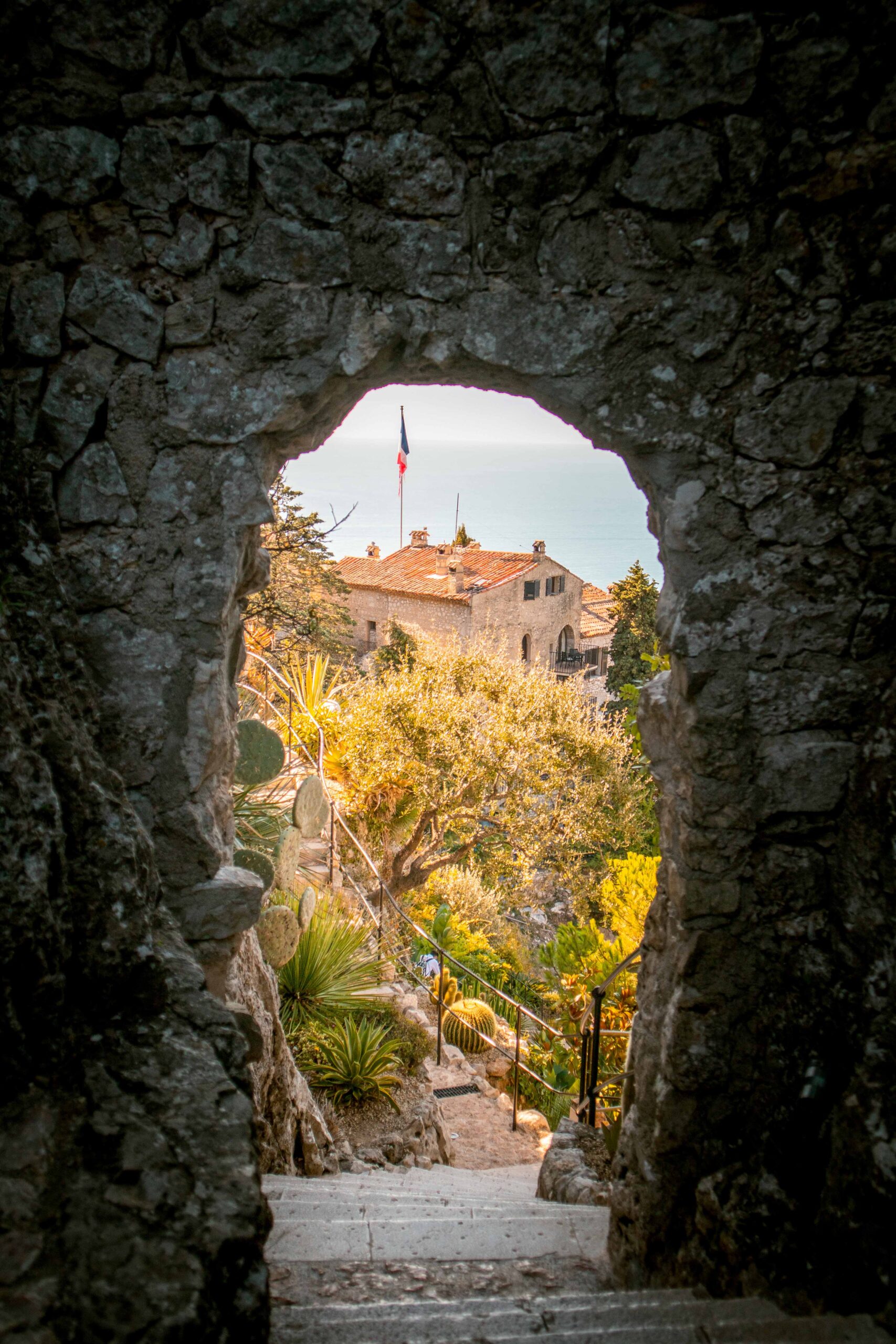 Staircase view of the Mediterranean sea and the Eze Exotic Garden on a sunny day from the window of a stone arch in Eze Village, France