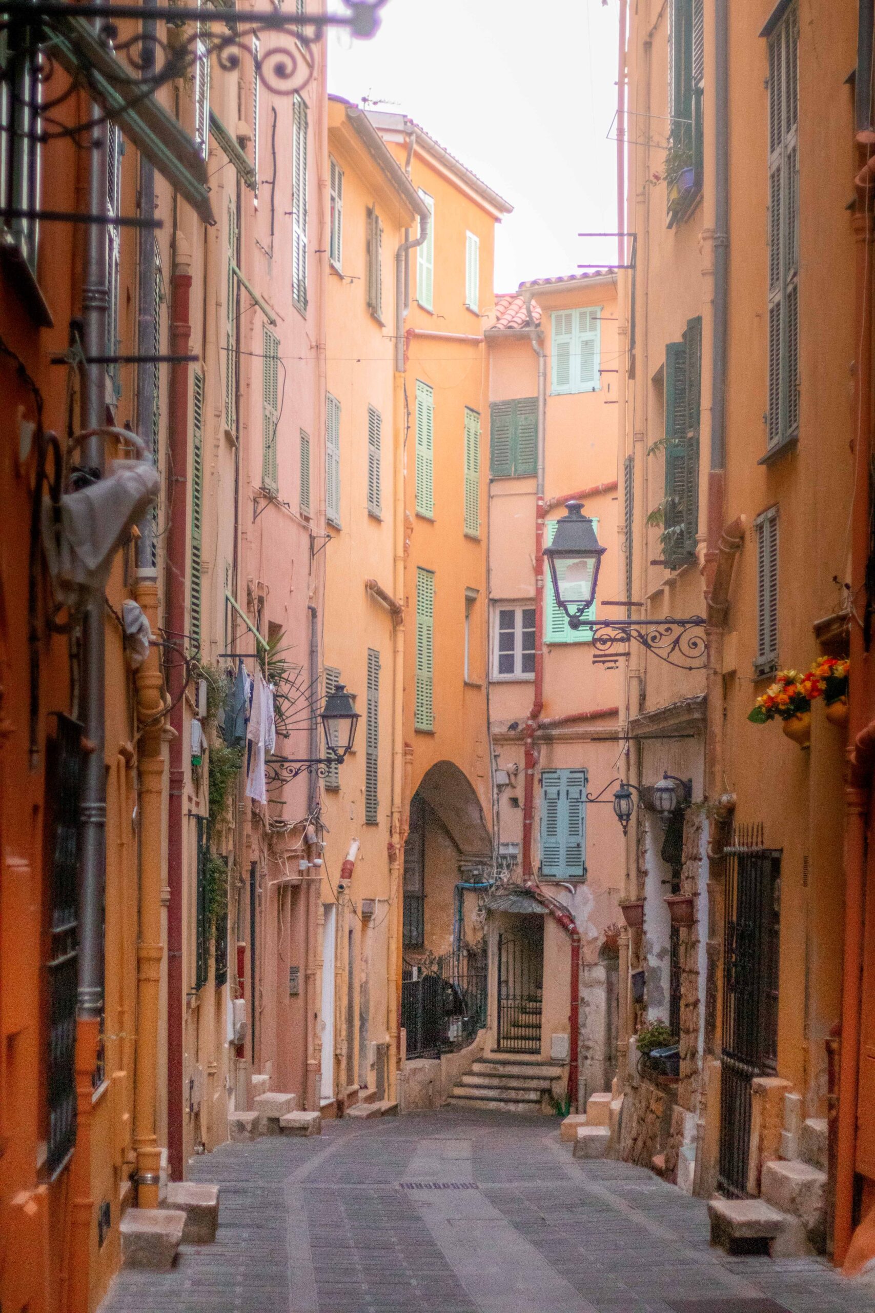 Colourful narrow street ("Rue Longue"), featuring orange, yellow and pink facades and painted blind windows in the Old Town of Menton, France