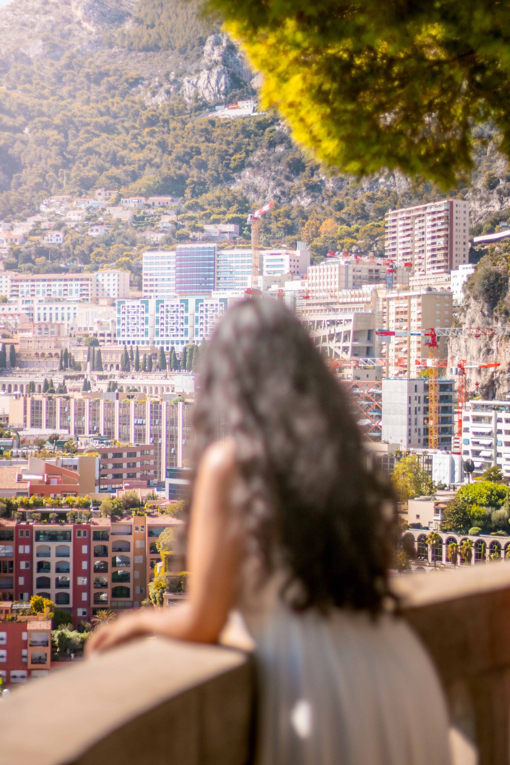 Woman wearing a white dress posing in a balcony at the Saint-Martin Gardens located on The Rock ("Le Rocher") during a sunny day in Monaco