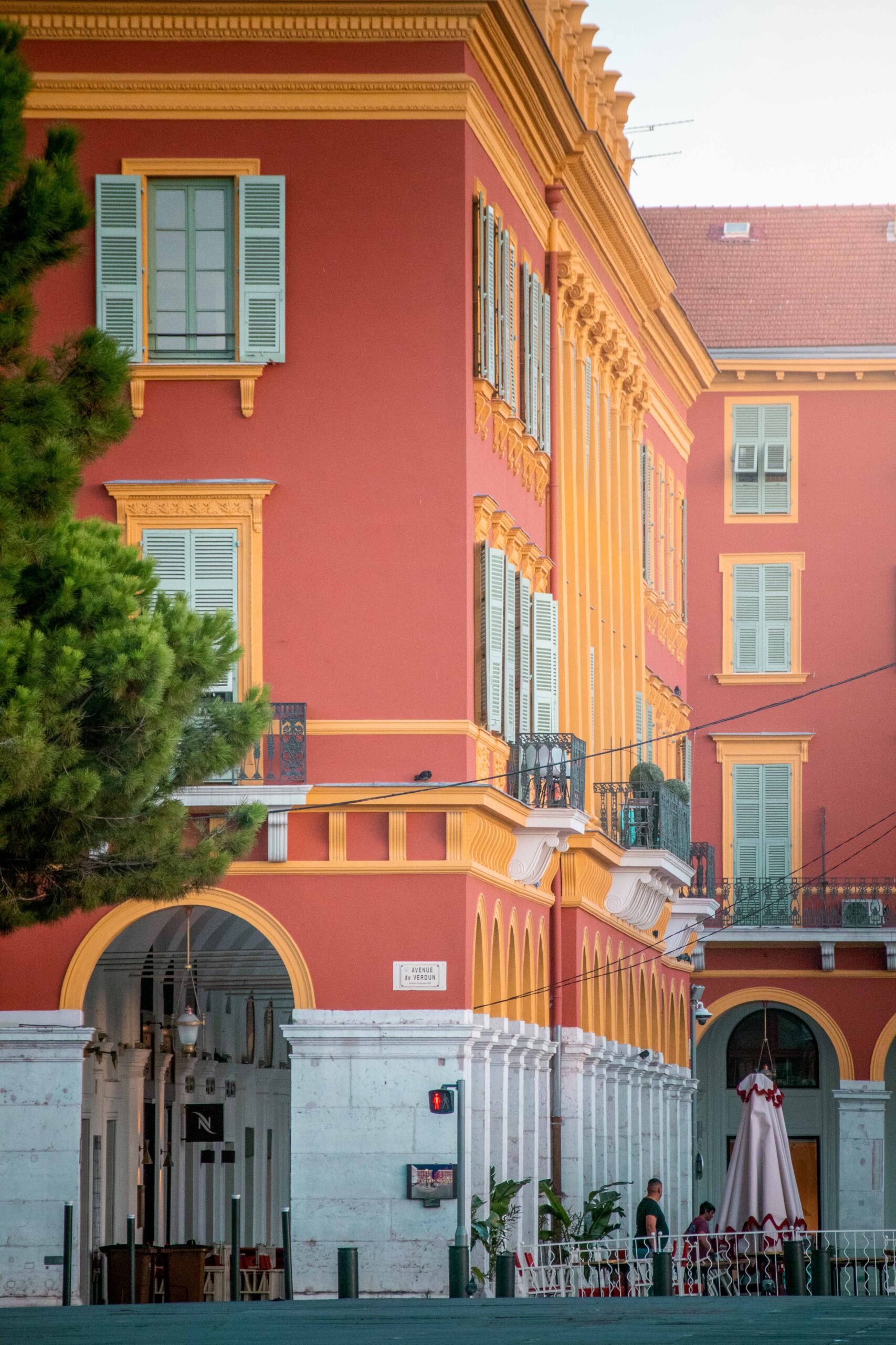 Red and yellow building (windows, balconies, lamps and arches) at the intersection of Avenue de Verdun and Place Masséna in Nice, France