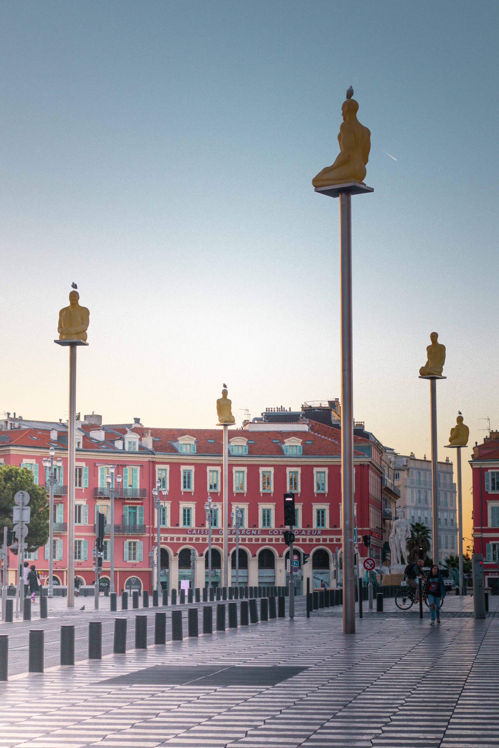 Pedestrians and statues of the artistic project "Conversation à Nice" during sunrise at Place Masséna in Nice, France