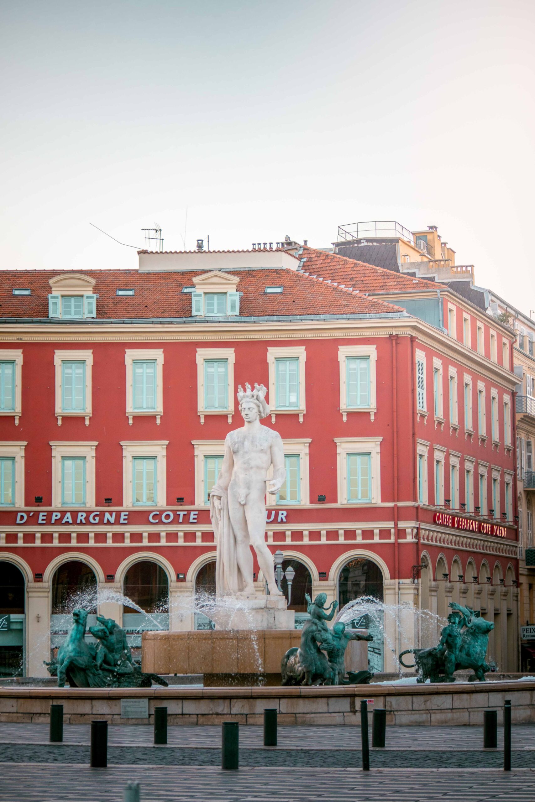 Statue of Apollo and red building facade during sunrise at Place Masséna in Nice, France