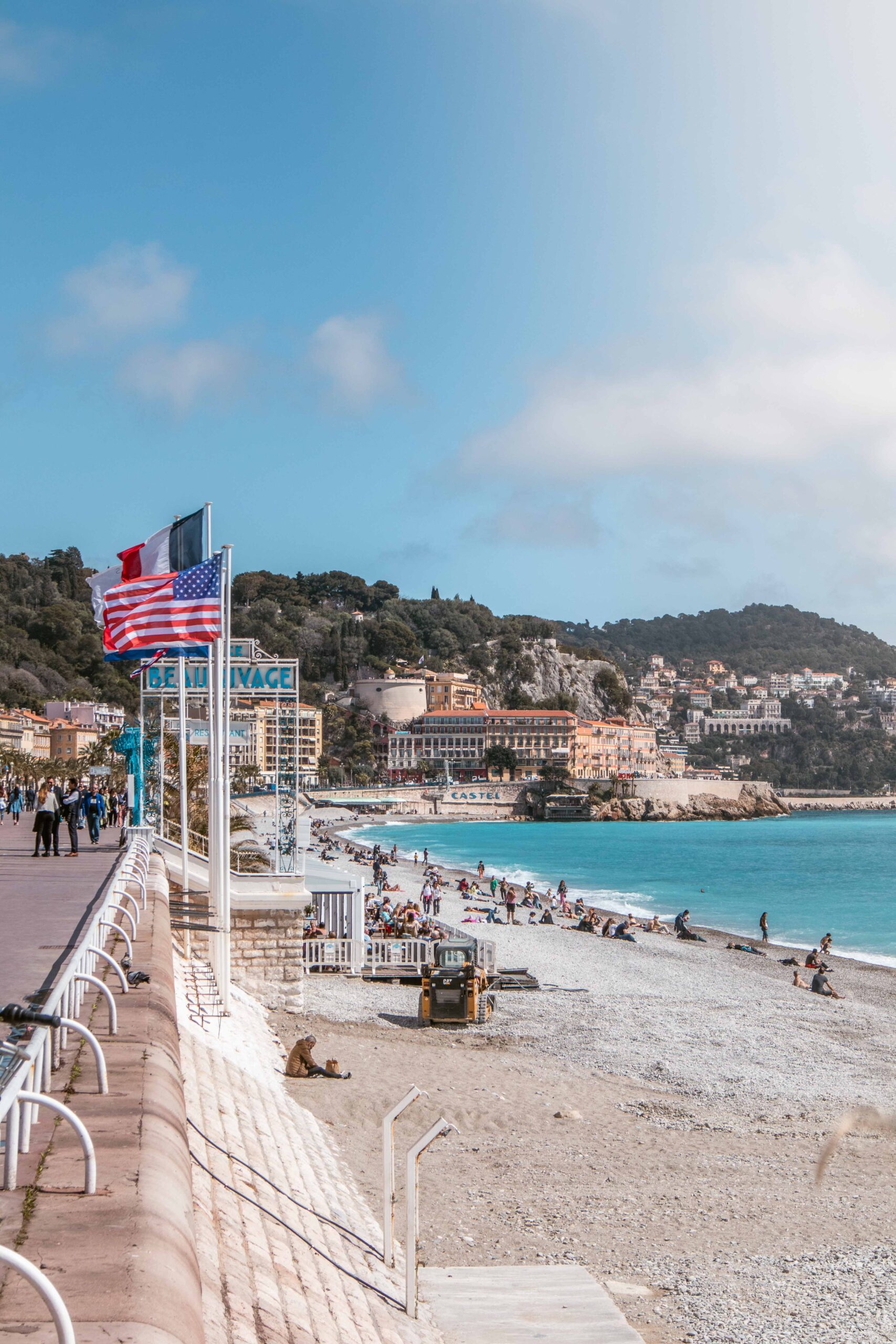 View of the pebble beach, the entrance of Le Beau Rivage private beach and the Colline du Château from the Promenade des Anglais in Nice, France