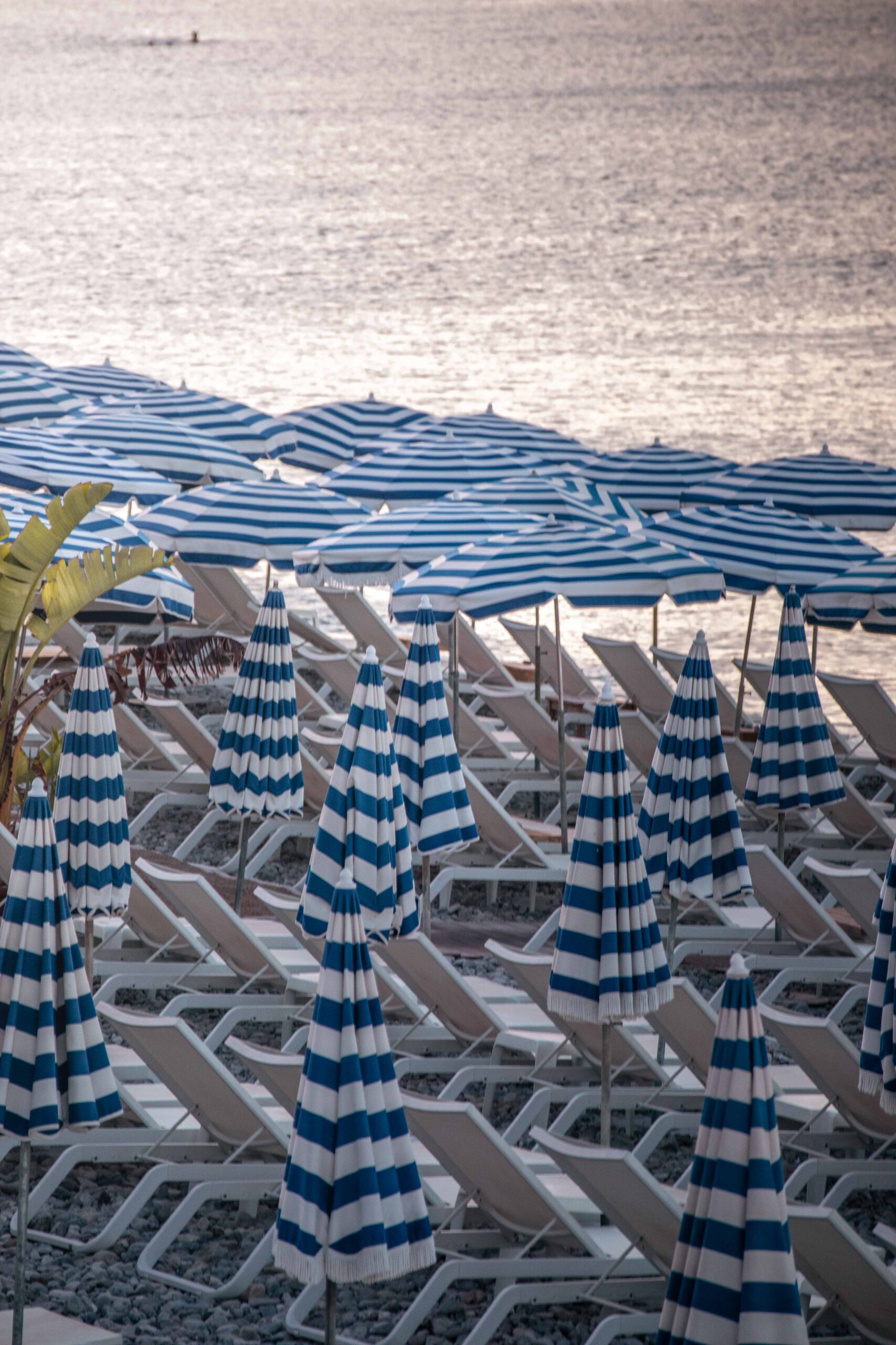 Blue and white beach umbrellas during sunrise at Ruhl plage along the Promenade des Anglais in Nice, France