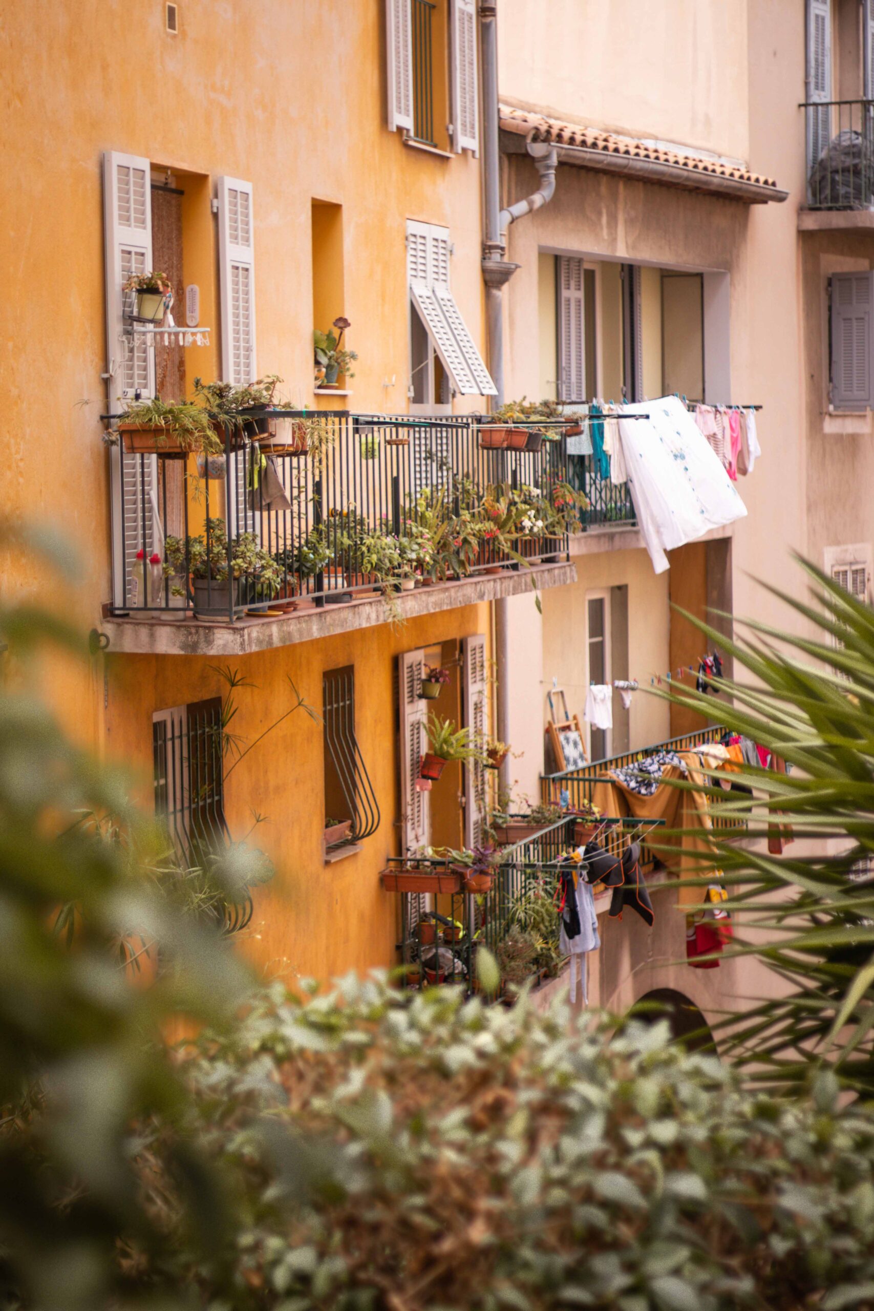 Hanging clothes drying and plants on the balcony of colourful buildings with orange and beige facades in the Old Town of Nice (Vieux-Nice) in Nice, France