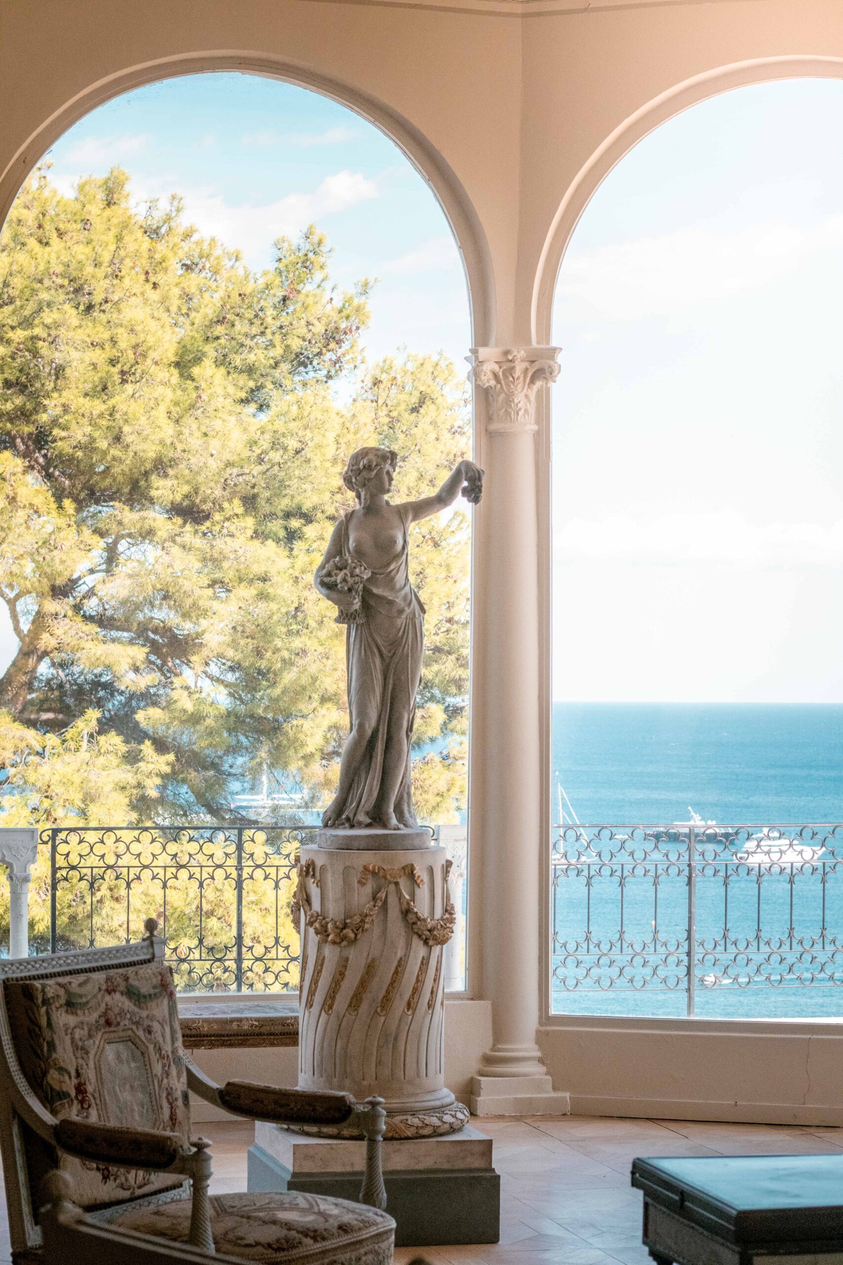 Indoor room of the Villa Ephrussi de Rothschild with a statue, a chair and a view over the Mediterranean sea on a sunny day in Saint-Jean-Cap-Ferrat, France