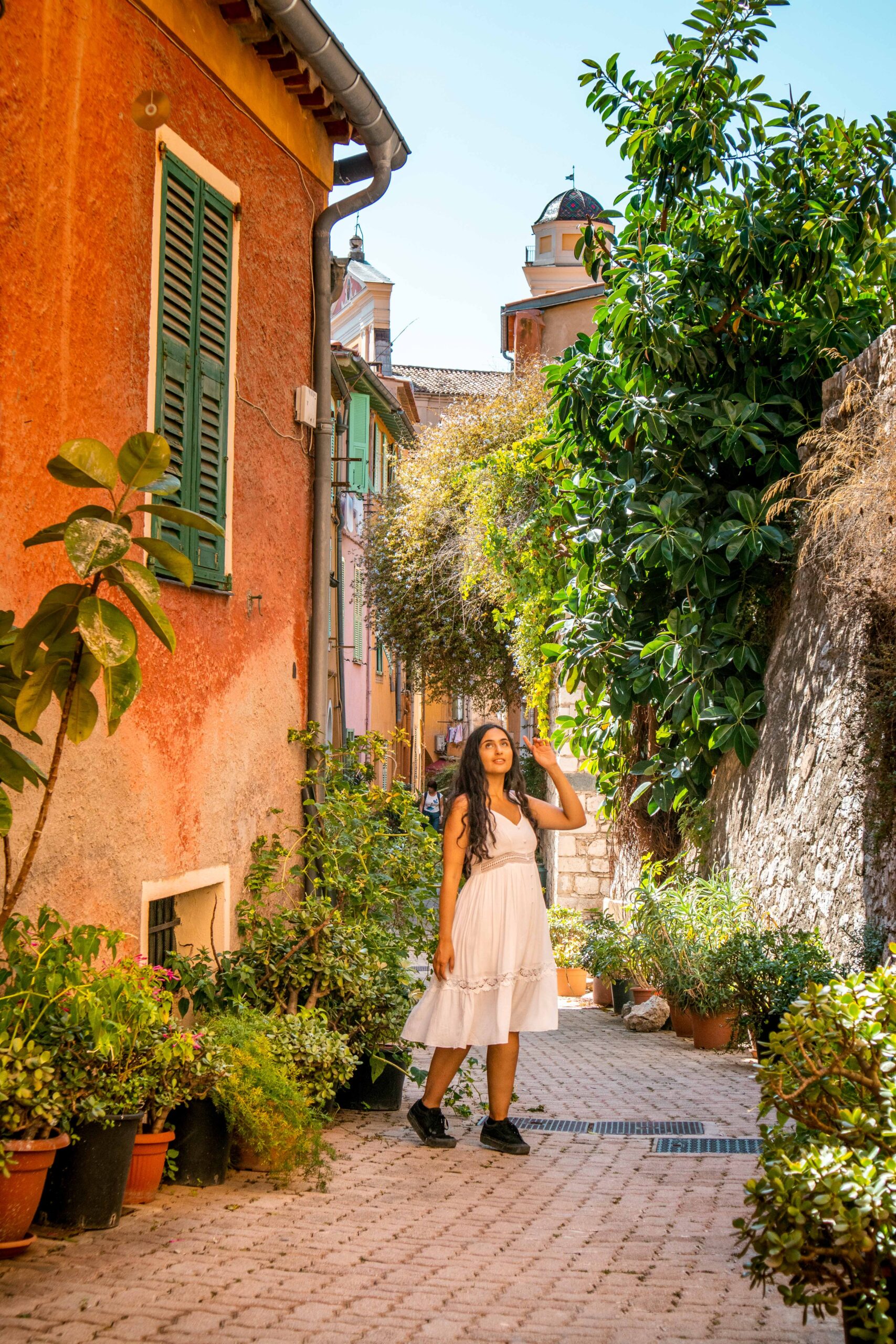 Woman wearing a white dress posing in a narrow and colourful street in the Old Town of Villefranche-sur-Mer, France